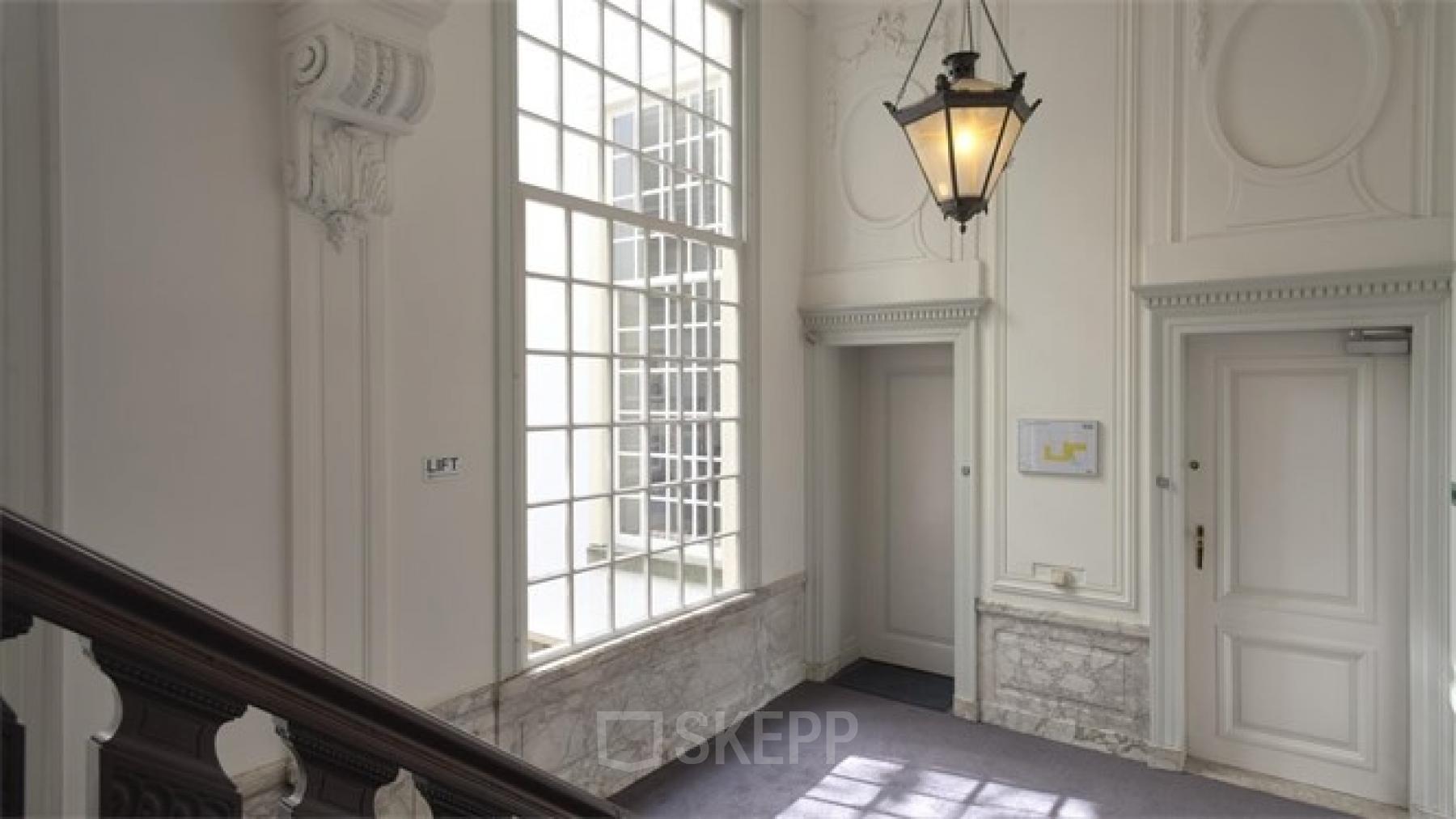 Interior view of Herengracht 495 office space rental, featuring a grand staircase, marble details, and an elegant hanging light in the Amsterdam Canal Belt.