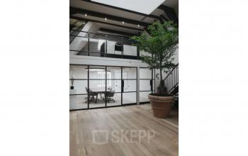 Modern office space rental available at Herengracht 168 in the Amsterdam Canal Belt. Features an open floor plan with large windows and a mezzanine level, ideal for dynamic work environments.