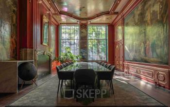 Elegant Amsterdam office space for rent at Herengracht 168 with a grand meeting table, ornate walls, and large windows offering views of the Canal Belt.
