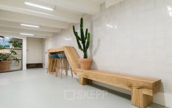 Modern office space rental at Herengracht 168 in Amsterdam Canal Belt, featuring a wooden bench and plants for a welcoming atmosphere.