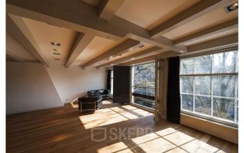 Spacious office area with large windows overlooking Amsterdam Canal Belt at Herengracht 168. Ideal for office space rental with natural light and wooden flooring.