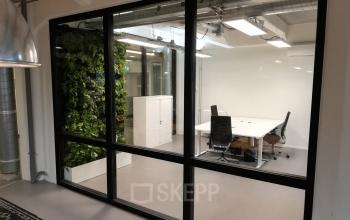 Modern office space with glass walls and a greenery wall, featuring a table with chairs, available for office space rental in Amsterdam Houthavens.