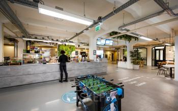 Spacious office area in Amsterdam Houthavens with a modern café setup, a foosball table, and a standing person at the counter, offering vibrant office space rental options.