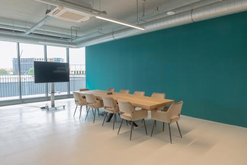 Modern conference room in office space rental at Koivistokade 68, Amsterdam Houthavens, Amsterdam, featuring a large wooden table, several chairs, large windows, and a presentation screen.