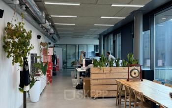 Office space for rent at Moermanskkade 303, Amsterdam Houthavens, featuring open workspaces with plants and natural light. Two people are working at desks.