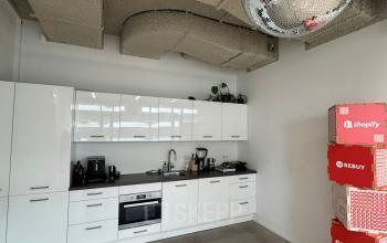 Modern kitchenette in an office space with sleek white cabinets and a disco ball ceiling feature, perfect for office space rental in Amsterdam Houthavens.