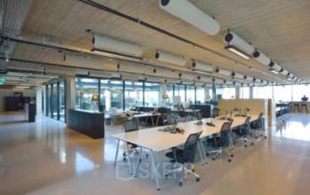 Modern office space rental at Archangelkade 9, Amsterdam Houthavens. Open floor plan with large desks, ergonomic chairs, ample lighting, and glass-walled meeting rooms.