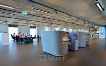 Modern office space at Archangelkade 9 in Amsterdam Houthavens with open plan layout and various workstations. Two people are working on computers, while another person is seated in a lounge area.