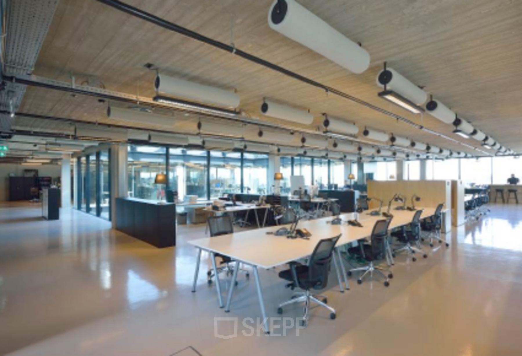Modern office space rental at Archangelkade 9, Amsterdam Houthavens. Open floor plan with large desks, ergonomic chairs, ample lighting, and glass-walled meeting rooms.