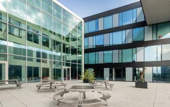 Exterior view of a modern office building at Pedro de Medinalaan 1-9, Amsterdam IJburg, featuring a spacious courtyard with bench seating. Ideal for office space rental.