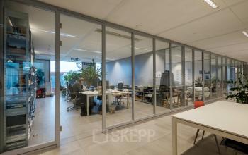 Modern office interior at Pedro de Medinalaan 7, Amsterdam IJburg, featuring glass partitions and a workspace with professionals engaged in business activities.