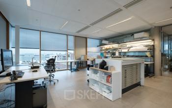 Spacious office space rental with desks and chairs, located at Pedro de Medinalaan 7 in Amsterdam IJburg, featuring large windows and a well-lit environment.