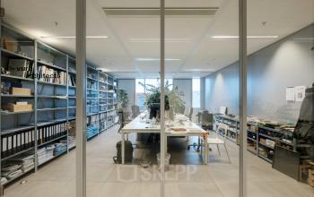 Modern office space at Pedro de Medinalaan 7, Amsterdam IJburg, featuring a long table, shelving with organized materials, and a bright, inviting atmosphere. Ideal for office space rental.