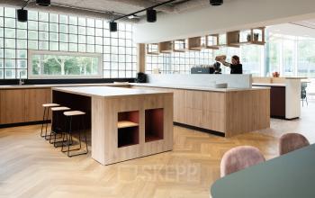Modern office space rental at Overschiestraat 65, Amsterdam New-West, featuring a well-equipped pantry area with professionals engaged in a conversation.