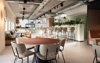 Modern office space for rent at Overschiestraat 63, Amsterdam New-West with a mix of seating options, including round tables, bar stools, and a comfortable lounge area with indoor plants.