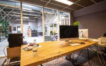 Modern workspace with wooden desk, computer monitors, and open glass partitions, located at Anthony Fokkerweg 3, Amsterdam Nieuw-West. Ideal office to rent for tech startups and creatives seeking inspiring environments.