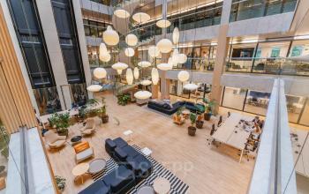 Spacious and modern open floor plan in office space rental at Koningin Wilhelminaplein 1, Amsterdam New-West. Features cozy seating areas, large wooden tables, and hanging lights, creating a welcoming work environment.