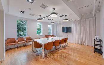 Spacious conference room at Koningin Wilhelminaplein 1, Amsterdam New-West, featuring a long table, leather chairs, large windows, and a TV screen. Ideal office space rental for productive meetings.