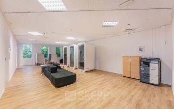 Spacious open area with wooden flooring at Koningin Wilhelminaplein 1, featuring furniture, soundproof pods, and large windows. Ideal for open floorplan office space rental in Amsterdam New-West.