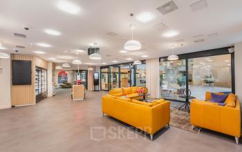 Spacious, modern lounge area at Koningin Wilhelminaplein 1, Amsterdam New-West, featuring vibrant yellow couches and a well-lit ambiance perfect for informal meetings. Ideal for those looking to rent office space.
