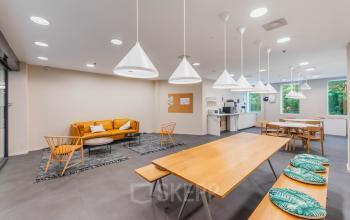 Bright and spacious lounge in Amsterdam New-West's Koningin Wilhelminaplein 1 with modern furnishings, ideal for office space rental, featuring cozy seating, a dining area, and a kitchenette.