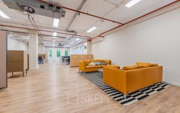 Spacious open floorplan at Koningin Wilhelminaplein 1, Amsterdam New-West, featuring modern sofas, wooden flooring, and ample natural light, ideal for office space rental.