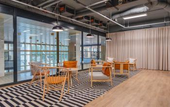 Stylish and modern lounge area with wooden furniture and cozy seating, featuring large windows overlooking Amsterdam's skyline. Perfect for a relaxed office space rental setting.