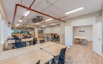 Open office space with modern decor and multiple workstations at Koningin Wilhelminaplein 1 in Amsterdam New-West, perfect for office space rental. Bright lighting and wooden floors enhance the ambiance.
