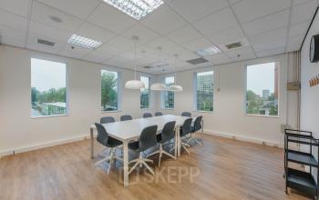 Bright conference room with large windows at Koningin Wilhelminaplein 1, Amsterdam. Spacious area includes a long table with modern chairs, perfect for office space rental. Ideal for small meetings or collaborative work.