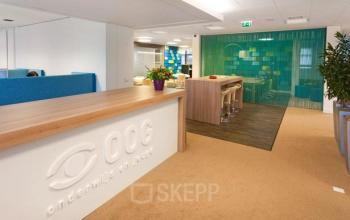 Modern office space with a reception desk, meeting area with high chairs, and colorful room dividers at Postjesweg 175 in Amsterdam Nieuw-West.