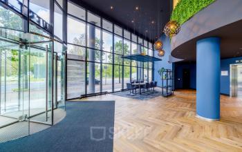 Modern office entrance with large glass doors, blue accents, and a seating area at Overschiestraat 61, Amsterdam New-West, ideal for office space rental.