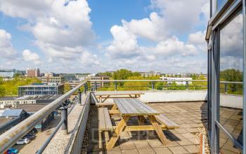 Rooftop terrace of an office building at Overschiestraat 61, Amsterdam Nieuw-West, featuring wooden picnic tables with a view of the surrounding business district.