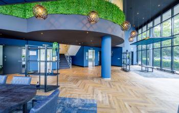 Modern entrance lobby of office space rental at Overschiestraat 61, Amsterdam Nieuw-West, featuring stylish seating, greenery, and wooden flooring.