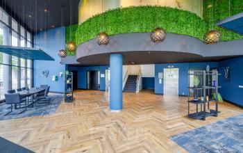 Spacious, modern lobby at Overschiestraat 61 with lush green accents, seating area, and stair access in Amsterdam New-West. Ideal for office space rental.