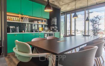 Bright office space with vibrant green kitchen cabinets, modern lighting, and a large table with chairs, ideal for office space rental in Amsterdam North.