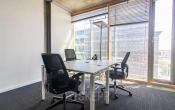 Bright office space with floor-to-ceiling windows and three ergonomic chairs surrounding a modern desk at Kraanspoor 12-58 in Amsterdam North. Ideal for office space rental.