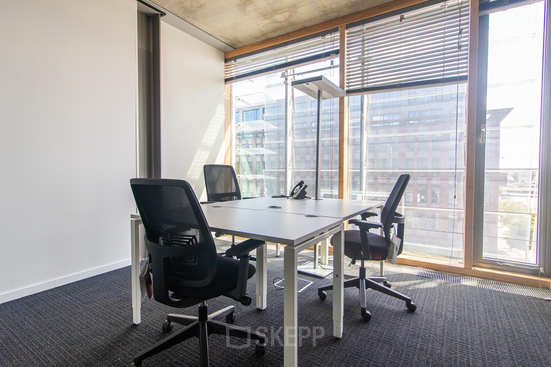 Bright office space with floor-to-ceiling windows and three ergonomic chairs surrounding a modern desk at Kraanspoor 12-58 in Amsterdam North. Ideal for office space rental.