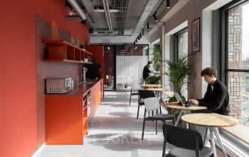 Amsterdam North office space rental with vibrant red interior and large windows, featuring people working on laptops and kitchen amenities.