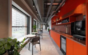 Bright office space with modern furniture, vibrant orange accents, and large windows, ideal for office space rental in Amsterdam North.