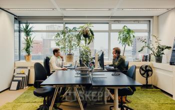 Bright office space at TT Vasumweg 44, Amsterdam North featuring modern furnishings, large windows, and professionals engaged in work at their desks.