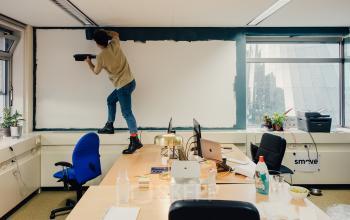 Office space with a person painting the wall, featuring desks and office supplies, available for rent at TT Vasumweg 44, Amsterdam North.