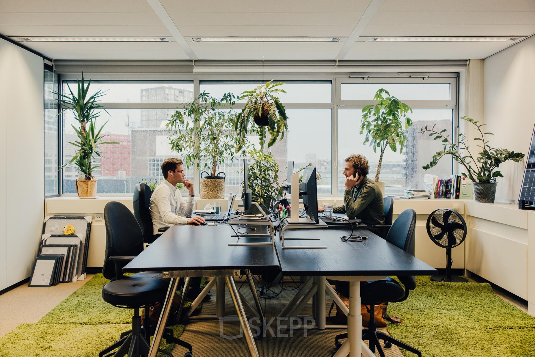 Bright office space at TT Vasumweg 44, Amsterdam North featuring modern furnishings, large windows, and professionals engaged in work at their desks.