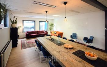 Bright office space in Amsterdam North featuring a large wooden table, stylish chairs, and lounge area. Ideal for collaborative work environments or meeting spaces with an inviting atmosphere for office space rental.