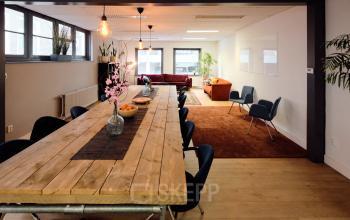 Spacious office interior at Hamerstraat 24, Amsterdam North, featuring a large wooden table with chairs, lounge area with couches, and bright windows, ideal for open floorplan office space rental.