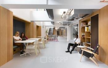 Modern office interior at Mt. Lincolnweg 38-40, Amsterdam North, featuring open workspaces with wooden elements, ample lighting, and colleagues engaged in discussions and laptop work—ideal for office space rental.