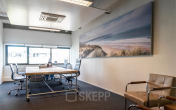 Modern office space rental at Asterweg 19, Servicepunt Kaap Noord, featuring a well-lit room with a large table, chairs, and tasteful artwork.