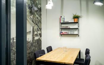 Cozy office space rental at Asterweg 19 in Amsterdam Noord with a wooden table, chairs, and shelving with plants and books.