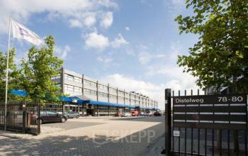 The exterior of the office building located at Distelweg 78-80, Amsterdam North, featuring a large modern structure with multiple floors and cars parked in front.