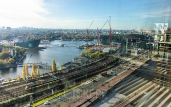 View from office to rent at Piet Heinkade 55, featuring Amsterdam East's skyline with a river, roads, and distant buildings.
