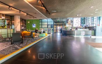 Spacious office lobby at Piet Heinkade 55, Amsterdam East, featuring modern furnishings and people engaging in business conversations, ideal for office space rental.